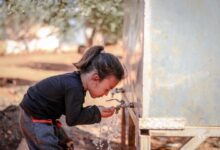 A little girl drinks water from a faucet outdoors in Idlib, Syria, representing hygiene and innocence.